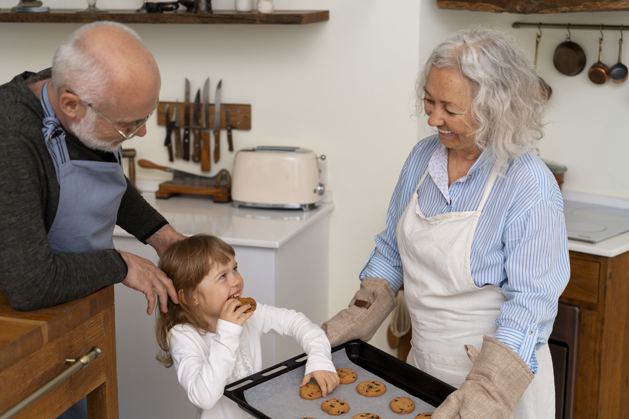 Une grand-mère fait goûter des cookies sortant du four à sa petite fille, le grand père la regarde affectueusement