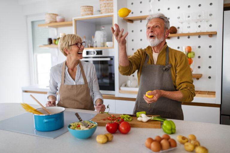 Faisant la cuisine, un homme âgé jongle avec des citrons. Une femme le regarde en riant