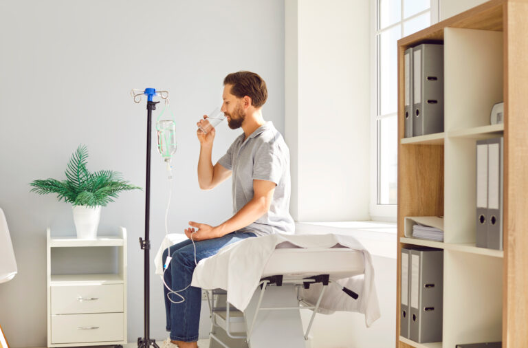 Un homme sous perfusion boit un verre d'eau